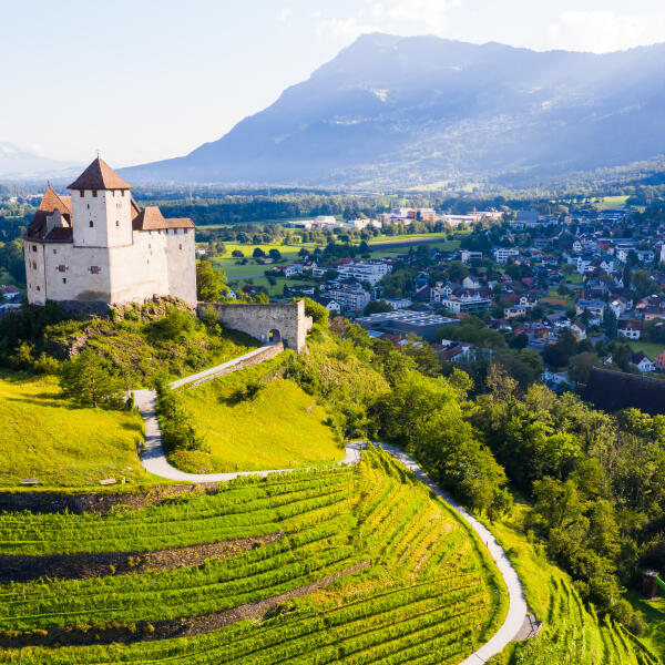 Aussicht von der Drohne von Stein Gutenberg Schloss auf grünem Hügel auf Hintergrund mit Kleinstadt Balzers, Liechtenstein